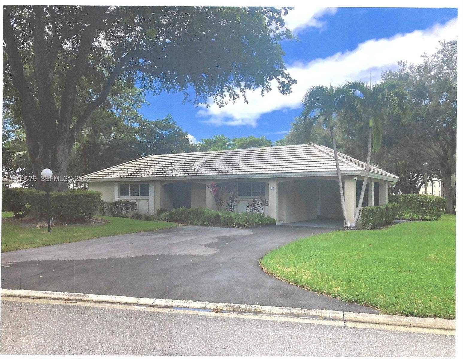 807 Cypress Boulevard, #V52, Pompano Beach, FL 33069 Single-story exterior featuring a gabled roofline, covered entryway, manicured lawn, paved driveway, and mature landscaping