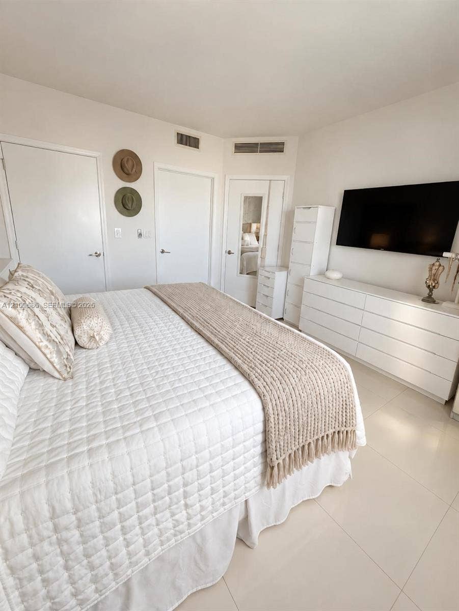 Neutral-toned interior featuring large-format tile flooring, multiple reach-in closets, and a built-in full-length mirror
