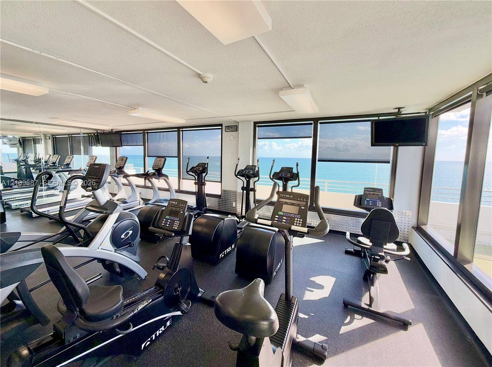 5555 Collins Avenue, #5C, Miami Beach, FL 33140 Fitness center featuring rubberized flooring, expansive floor-to-ceiling windows, and wall-mounted televisions