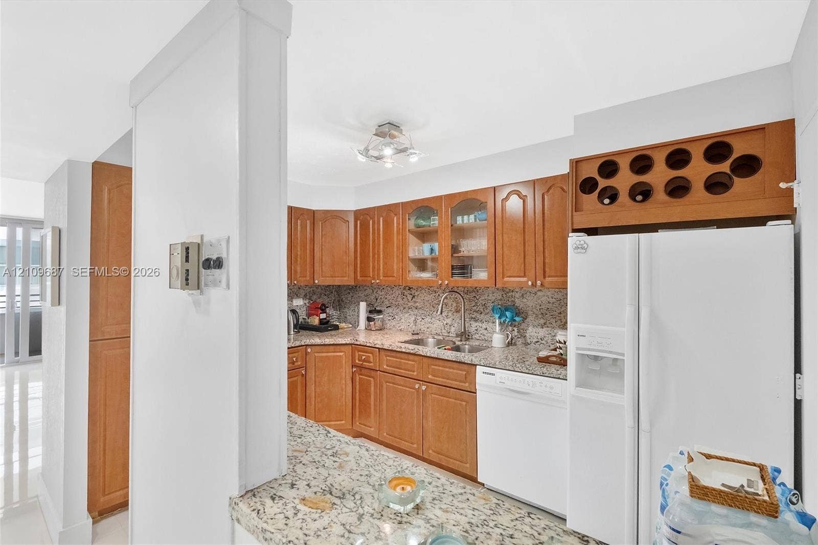 5555 Collins Avenue, #5C, Miami Beach, FL 33140 Kitchen featuring wood cabinetry, stone-surface countertops, built-in wine storage, a stainless steel sink with a high-arch faucet, and an integrated dishwasher