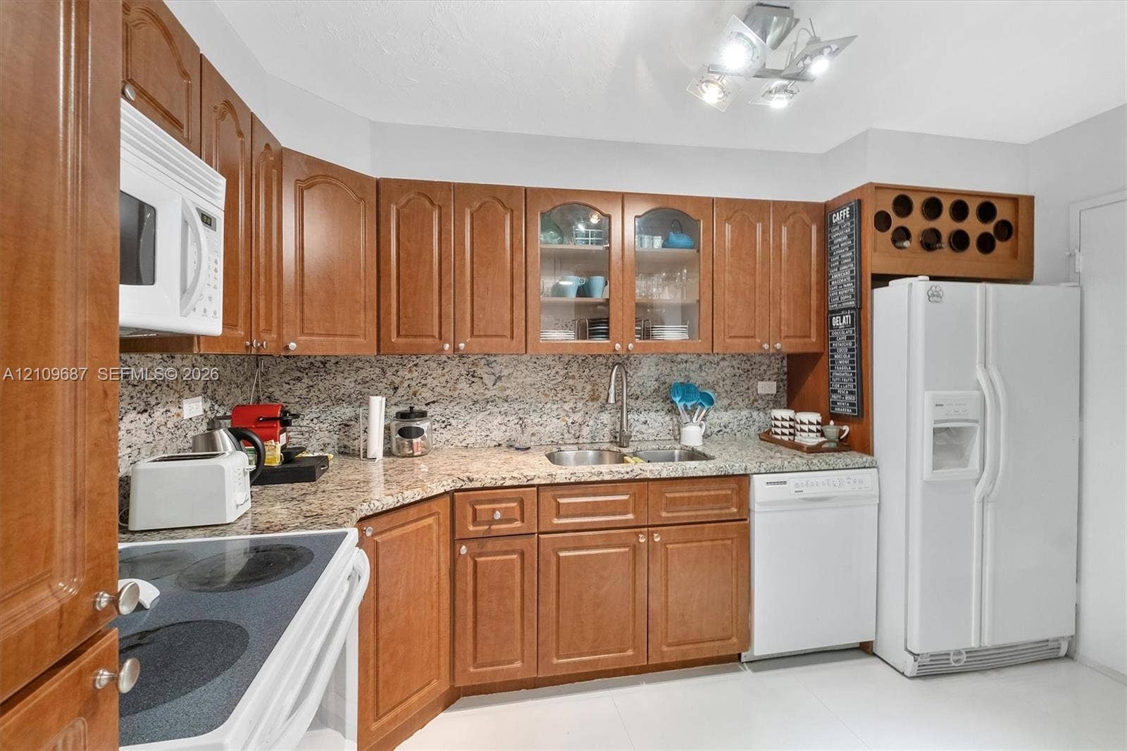5555 Collins Avenue, #5C, Miami Beach, FL 33140 Kitchen featuring wood cabinetry, stone countertops, glass-front upper cabinet doors, built-in wine storage, and a stainless steel double-basin sink