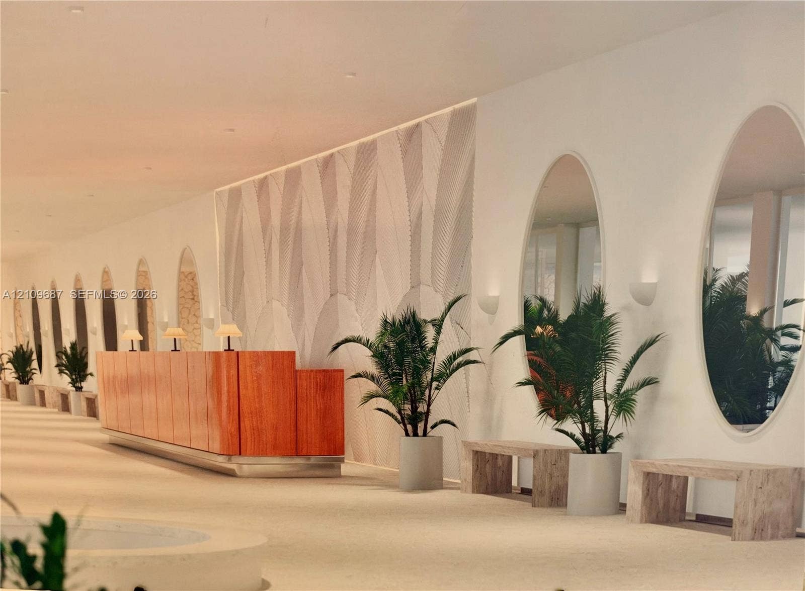 5555 Collins Avenue, #5C, Miami Beach, FL 33140 Grand lobby featuring a custom wood-paneled reception desk, full-height oval wall mirrors, decorative wall texturing, and recessed wall-mounted lighting