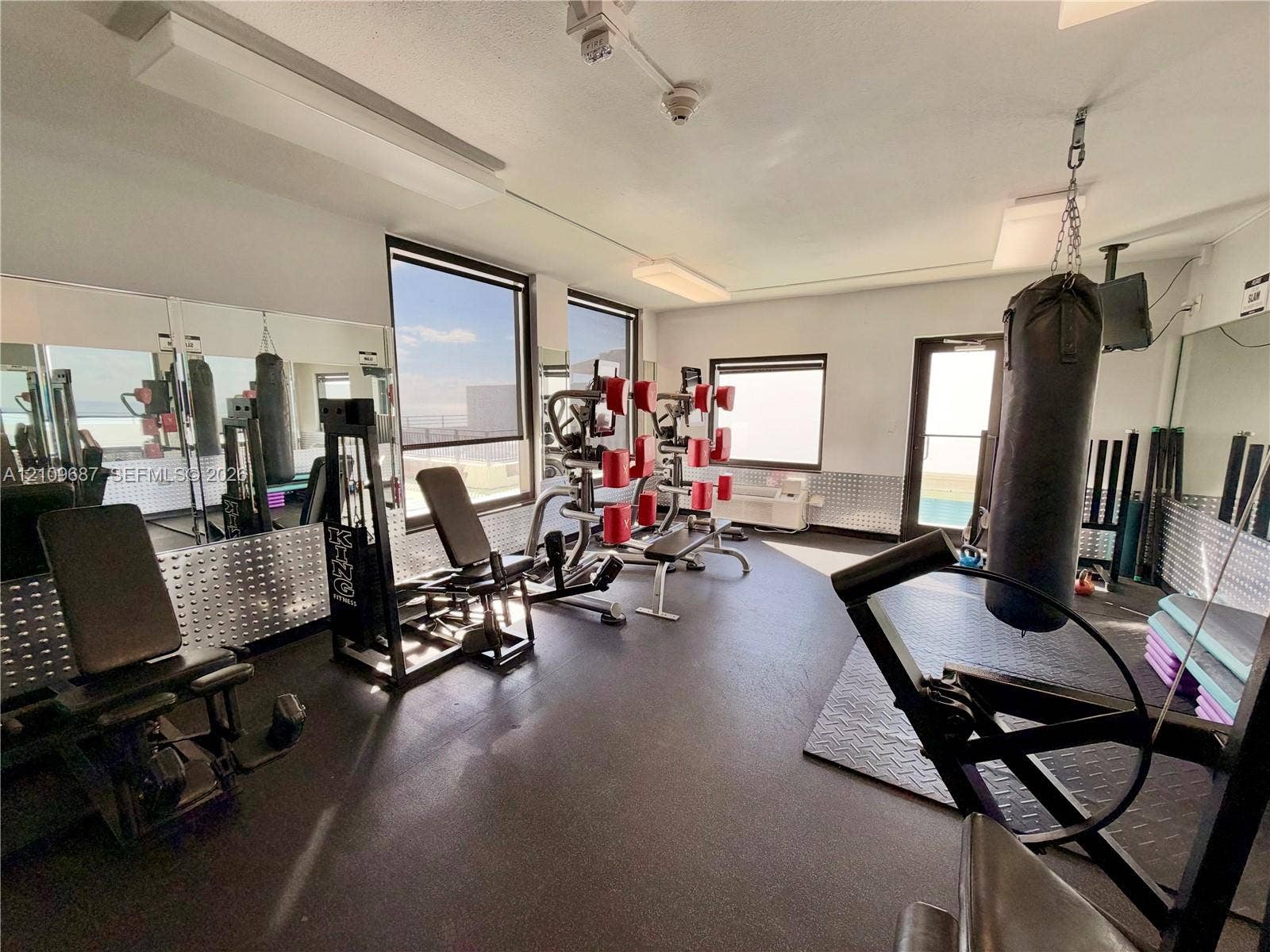 5555 Collins Avenue, #5C, Miami Beach, FL 33140 Fitness room featuring expansive mirror walls, rubberized flooring, diamond-plate metal wainscoting, and large windows