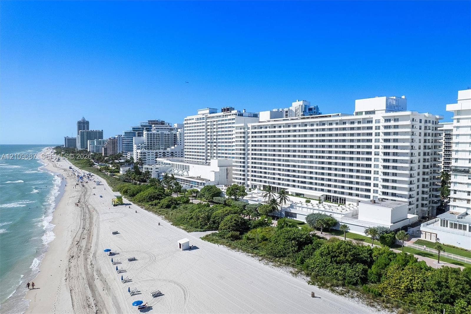 5555 Collins Avenue, #5C, Miami Beach, FL 33140 Coastal high-rise building with white stucco facade, expansive balcony tiers, direct beachfront access, and mature landscaping