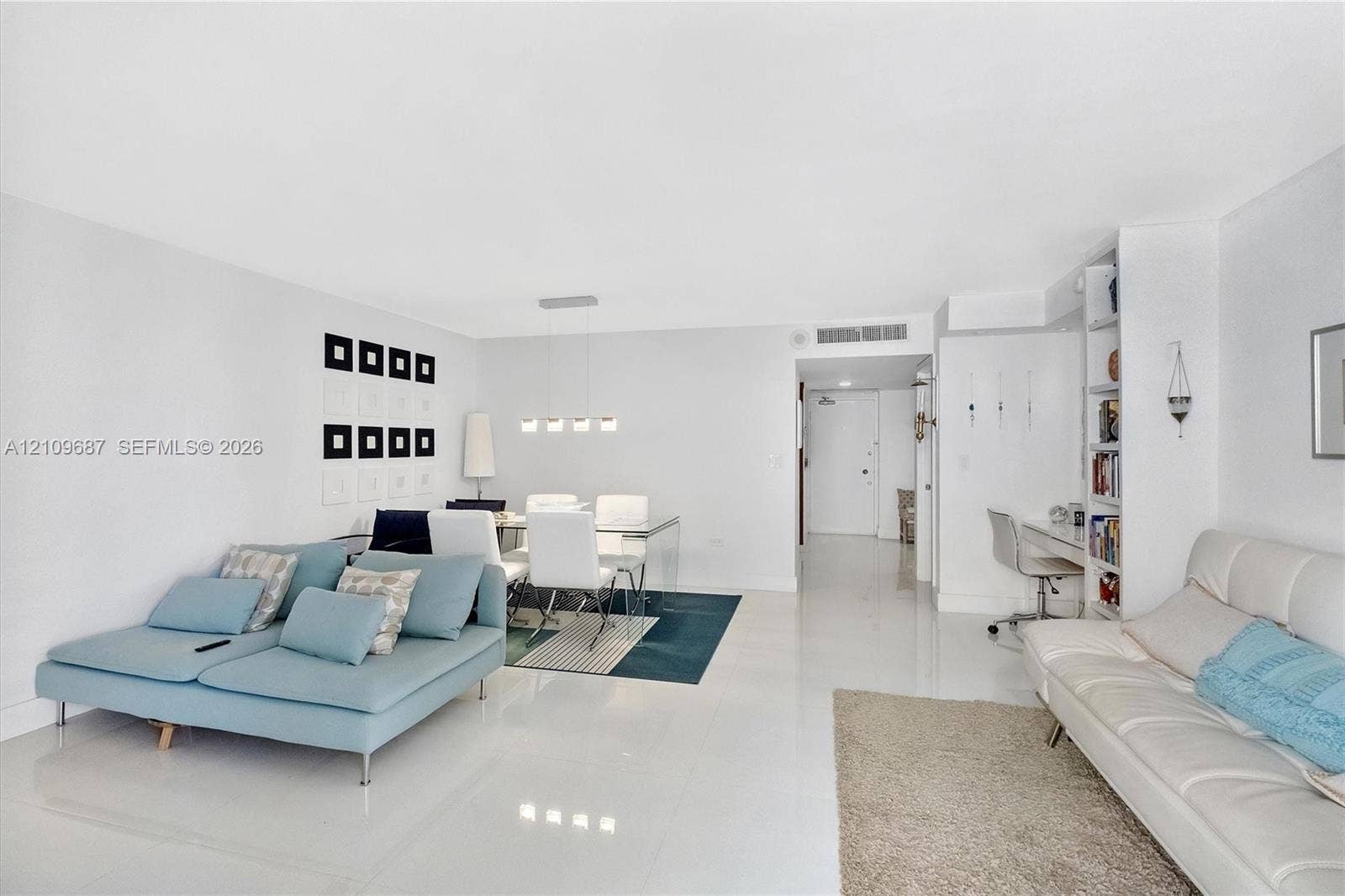5555 Collins Avenue, #5C, Miami Beach, FL 33140 Open-concept living space featuring high-gloss tile flooring, recessed lighting, a modern multi-light linear pendant fixture, and built-in floor-to-ceiling shelving