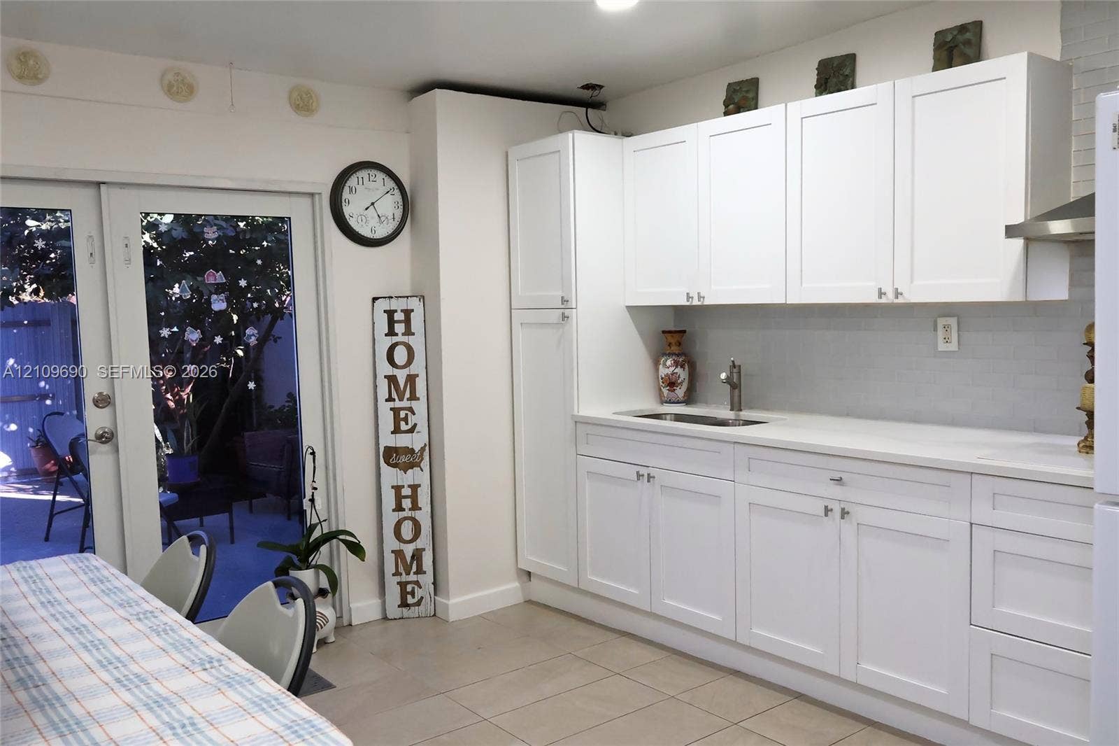 Kitchenette featuring white Shaker-style cabinetry, a stone-surface countertop, an integrated sink with a gooseneck faucet, a light-toned tile backsplash, and glass-paned double doors