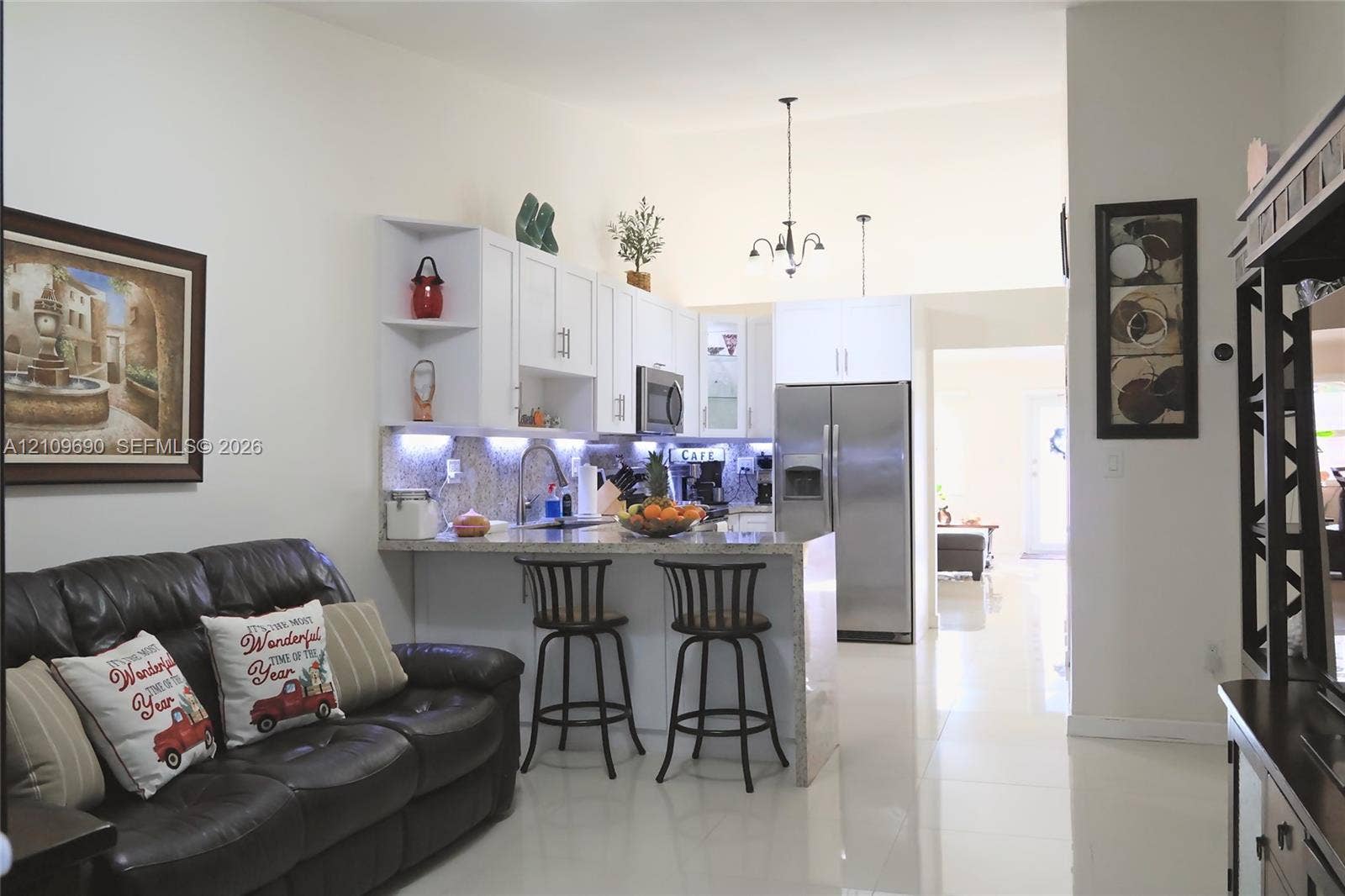 Kitchen featuring white cabinetry, stone-surface countertops, stainless steel appliances, under-cabinet lighting, and a breakfast bar