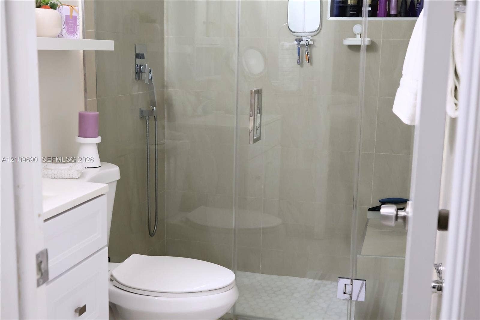 Walk-in shower featuring a frameless glass door, wall-mounted chrome hand-held shower head, integrated tiled shower bench, and pebble-style floor tiling