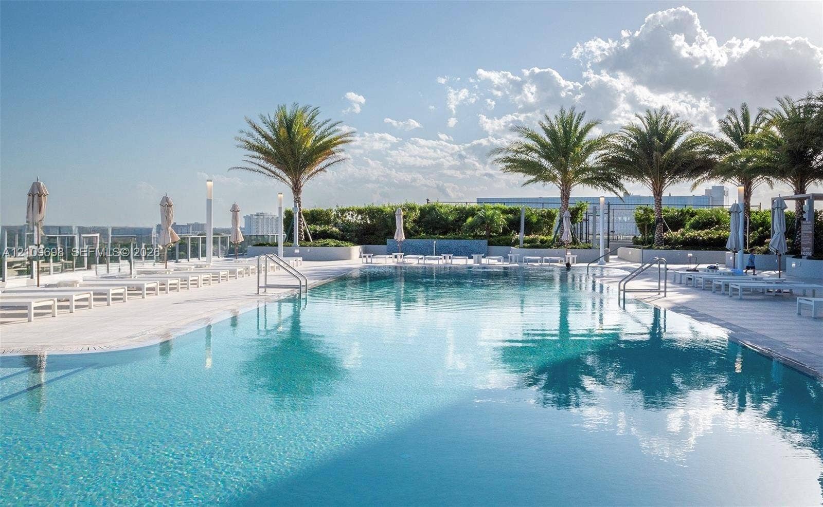 2411 Laguna Circle, #810, North Miami, FL 33181 Rooftop swimming pool featuring stone tile decking, perimeter glass railing, built-in water feature, and mature palm trees