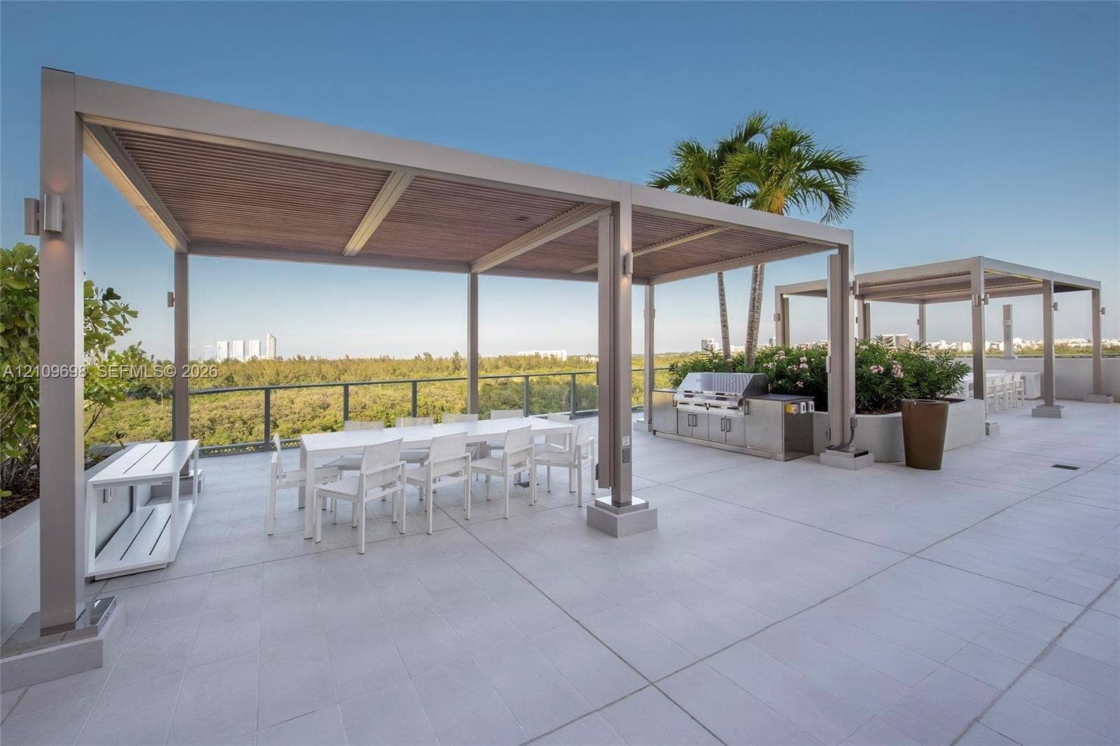 2411 Laguna Circle, #810, North Miami, FL 33181 Rooftop terrace featuring large-format tile flooring, dual metal-framed pergolas with wood-finish ceilings, a built-in stainless steel outdoor kitchen, and a glass-panel railing system