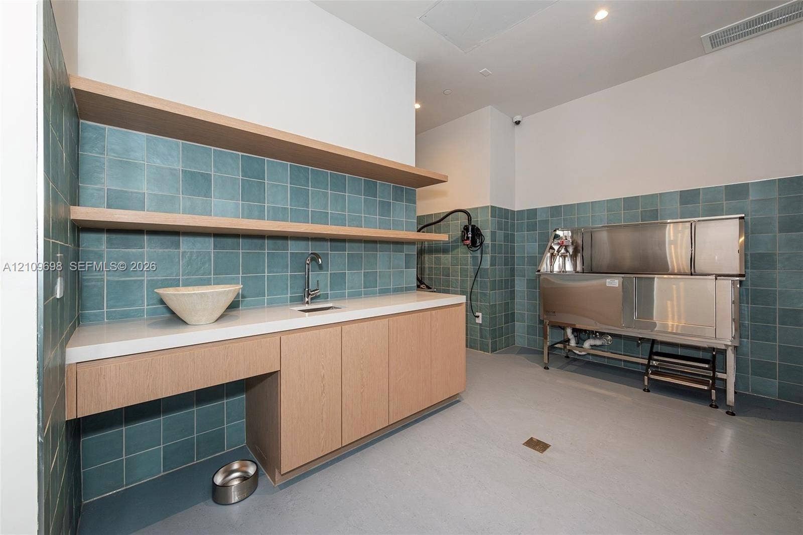 2411 Laguna Circle, #810, North Miami, FL 33181 Utility space featuring custom wood cabinetry, quartz countertops, blue square tile wall backsplash, open floating shelving, and a stainless steel washing station