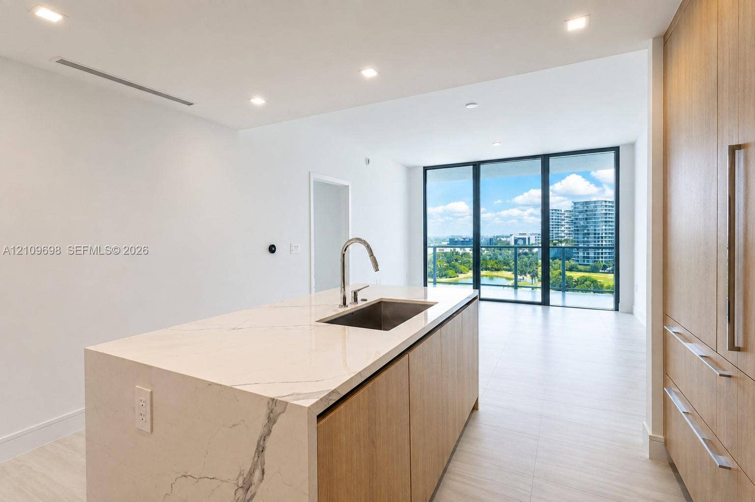 2411 Laguna Circle, #810, North Miami, FL 33181 Kitchen island with stone-finish waterfall countertop, undermount stainless steel sink, wood-finish cabinetry, recessed lighting, and floor-to-ceiling glass paneling
