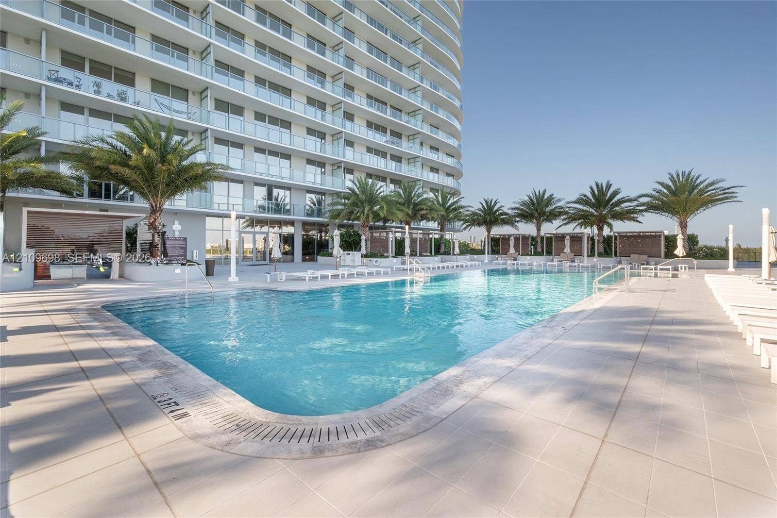 2411 Laguna Circle, #810, North Miami, FL 33181 Large swimming pool with tiled surround, palm tree landscaping, and built-in outdoor kitchen area