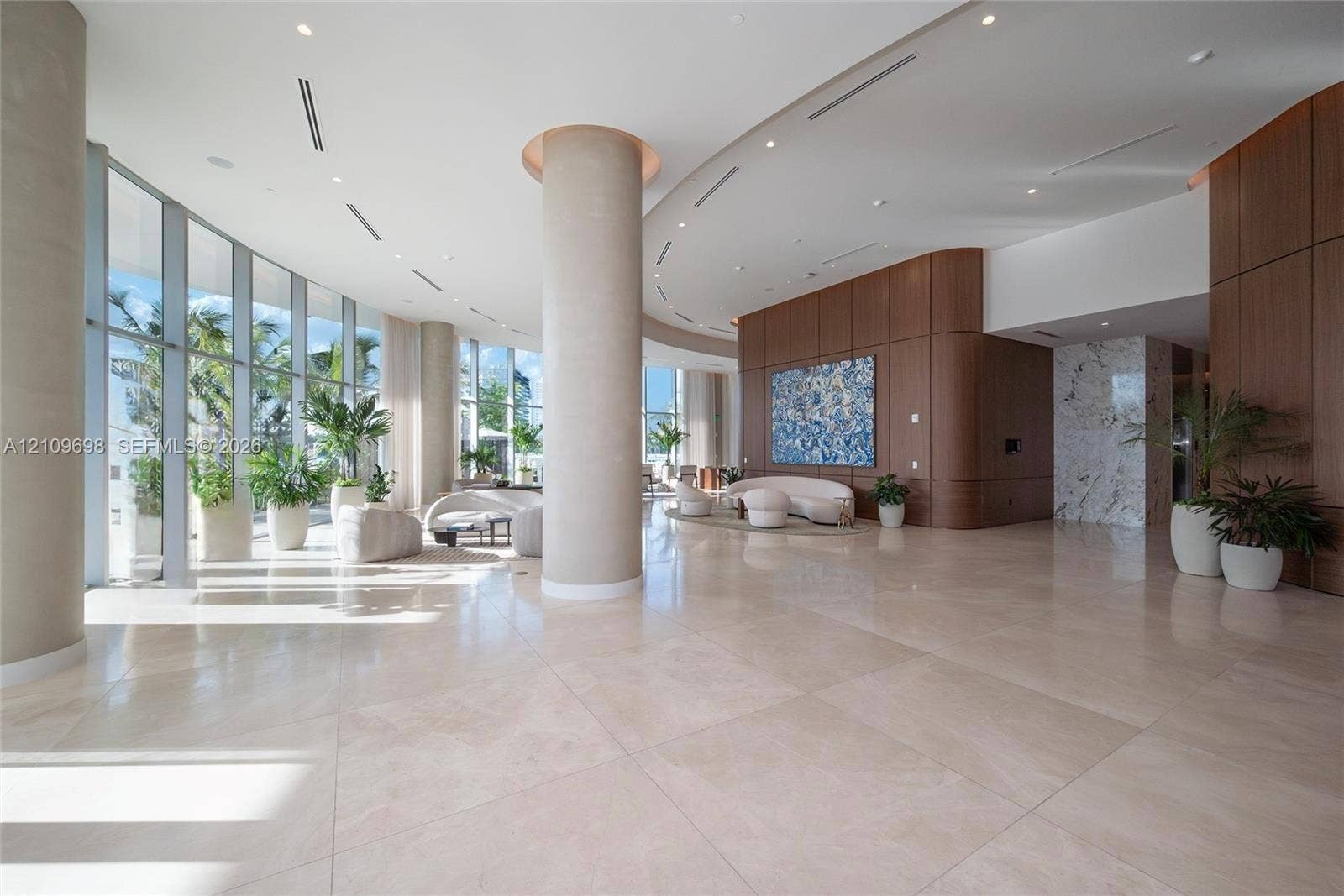 2411 Laguna Circle, #810, North Miami, FL 33181 Expansive interior space featuring floor-to-ceiling windows, polished stone flooring, curved architectural pillars, wood-panelled accent walls, and recessed ceiling lighting