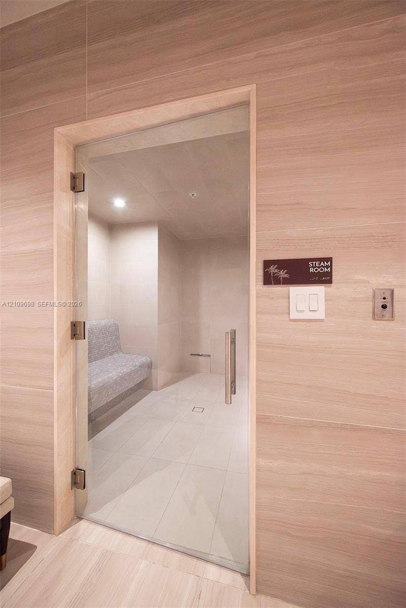 2411 Laguna Circle, #810, North Miami, FL 33181 Steam room featuring large-format tile wall cladding, a frameless glass door with brushed-metal hardware, an integrated tiled bench, and recessed ceiling lighting
