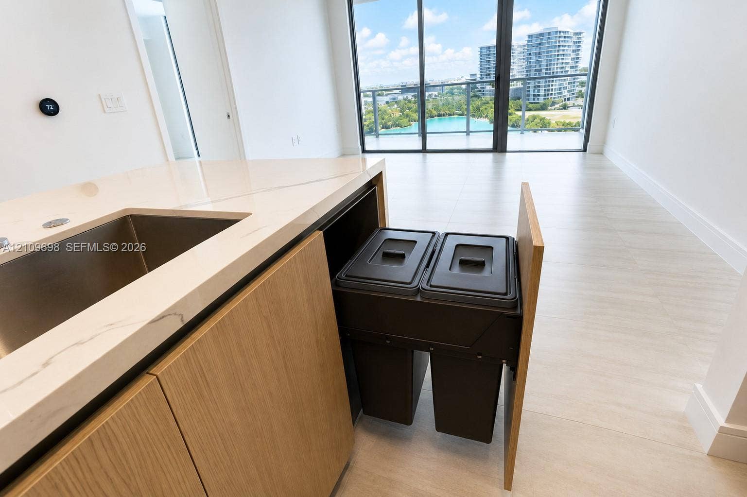 2411 Laguna Circle, #810, North Miami, FL 33181 Kitchen island featuring stone-finish countertops, an undermount sink, built-in dual waste disposal cabinetry, and light-tone flooring