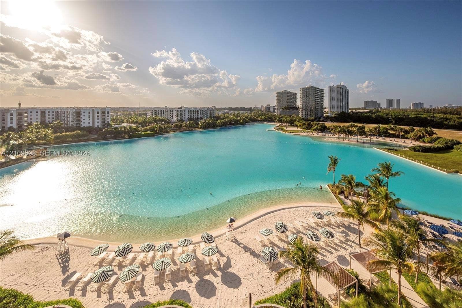 2411 Laguna Circle, #810, North Miami, FL 33181 Extensive turquoise lagoon featuring a white sand beach, surrounding palm trees, and structural shaded areas
