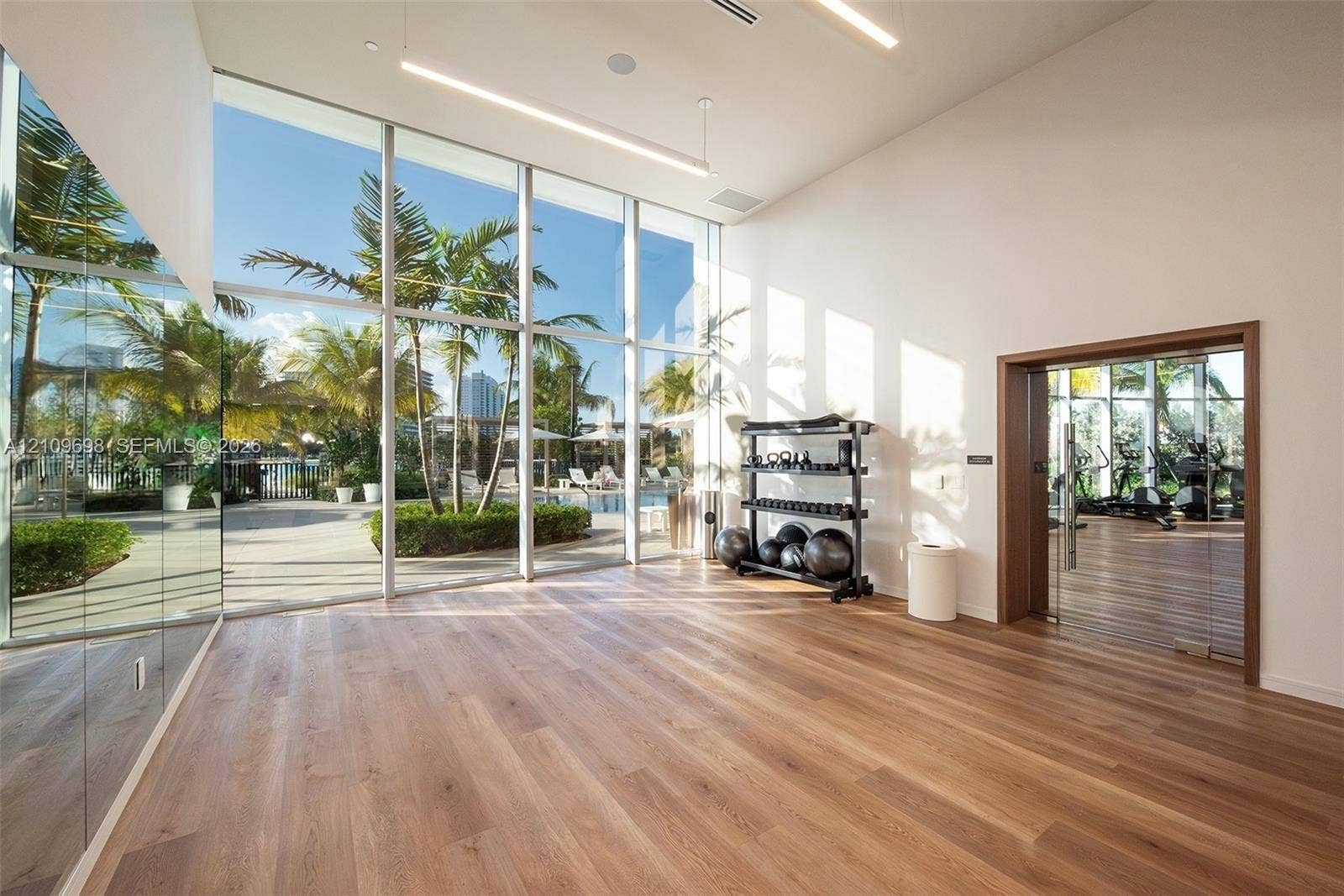 2411 Laguna Circle, #810, North Miami, FL 33181 Floor-to-ceiling windows, wood-finish flooring, full-wall mirrors, recessed linear lighting, and glass-paneled entry door