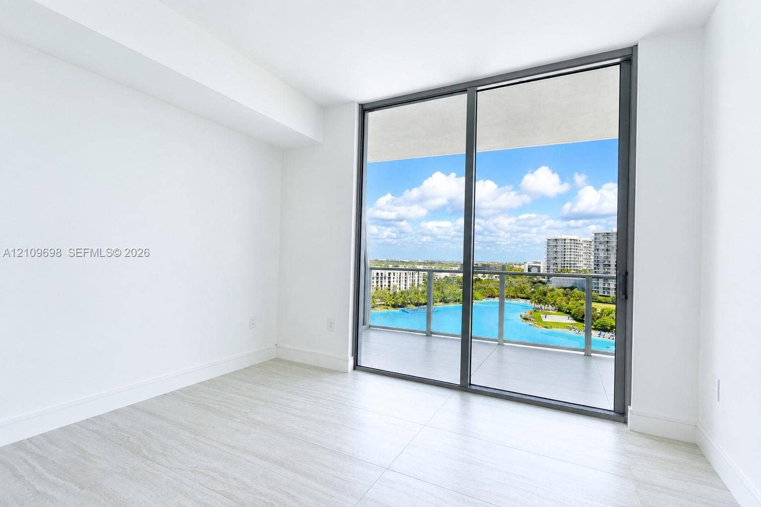 2411 Laguna Circle, #810, North Miami, FL 33181 Interior space featuring floor-to-ceiling sliding glass doors, neutral tile flooring, and a covered balcony with a glass railing