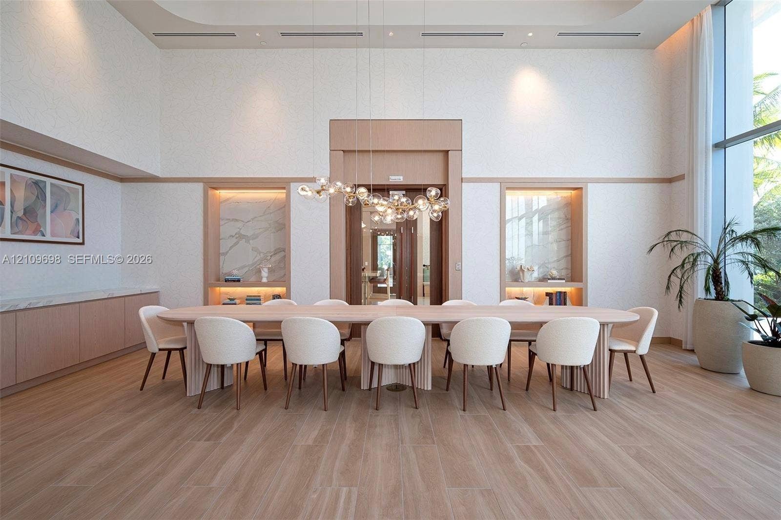2411 Laguna Circle, #810, North Miami, FL 33181 High-ceilinged room featuring wood-finish flooring, dual built-in shelving niches with stone-slab backsplashes, custom millwork, and an intricate multi-globe chandelier