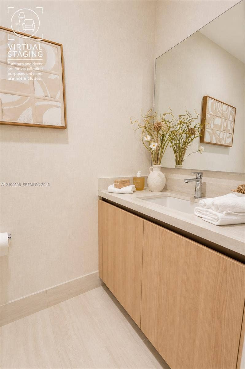 2411 Laguna Circle, #810, North Miami, FL 33181 Floating vanity with light wood-finish cabinetry, stone-style countertop, integrated sink, chrome faucet, and expansive frameless wall mirror