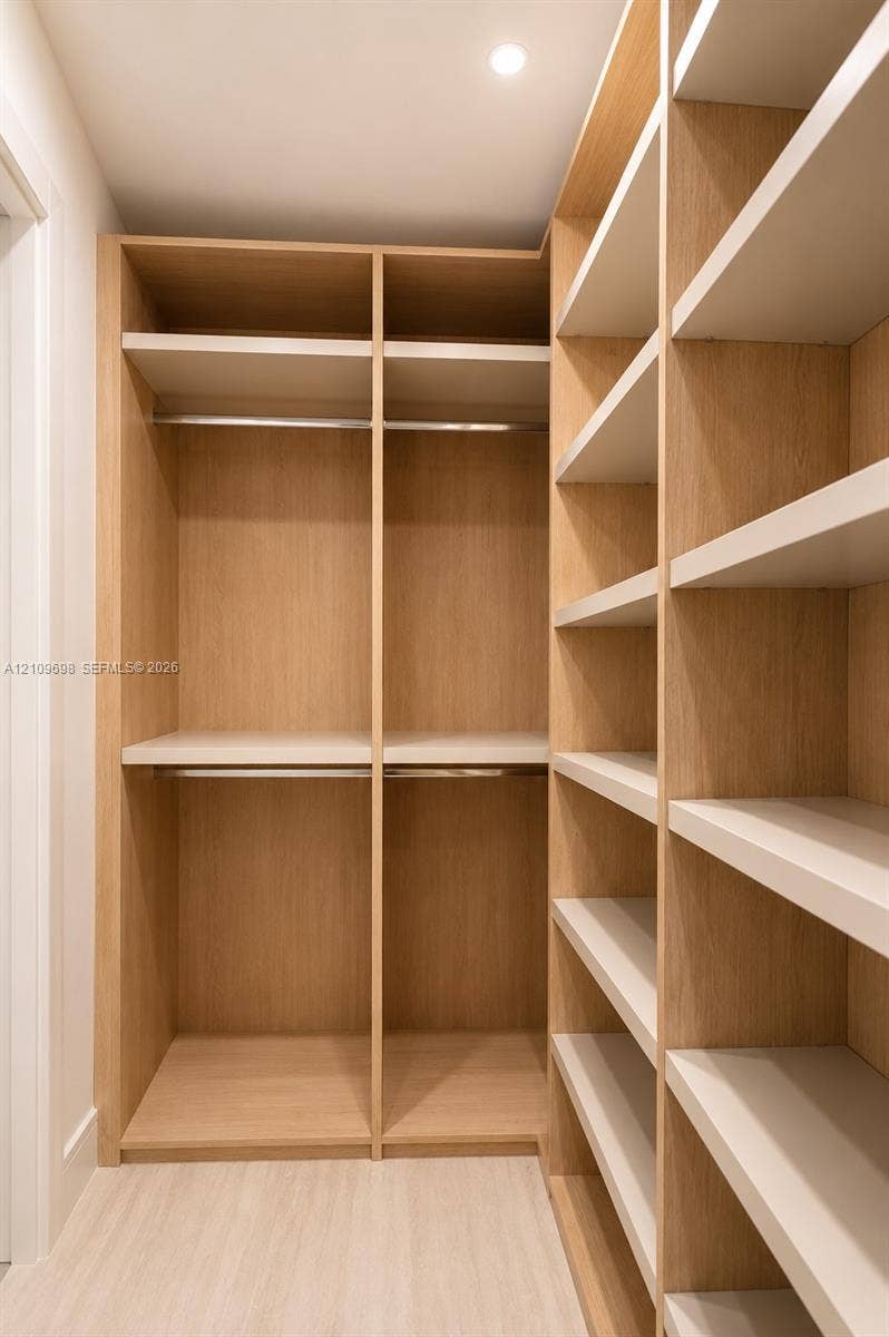 2411 Laguna Circle, #810, North Miami, FL 33181 Customized reach-in closet featuring light wood-finish cabinetry, built-in shelving units, integrated metal hanging rods, and recessed ceiling lighting