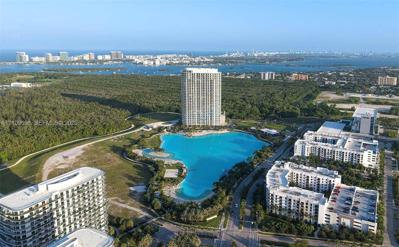 2411 Laguna Circle, #810, North Miami, FL 33181 Aerial perspective featuring a high-rise residential structure, a large-scale lagoon-style water feature, and expansive green space with mature trees
