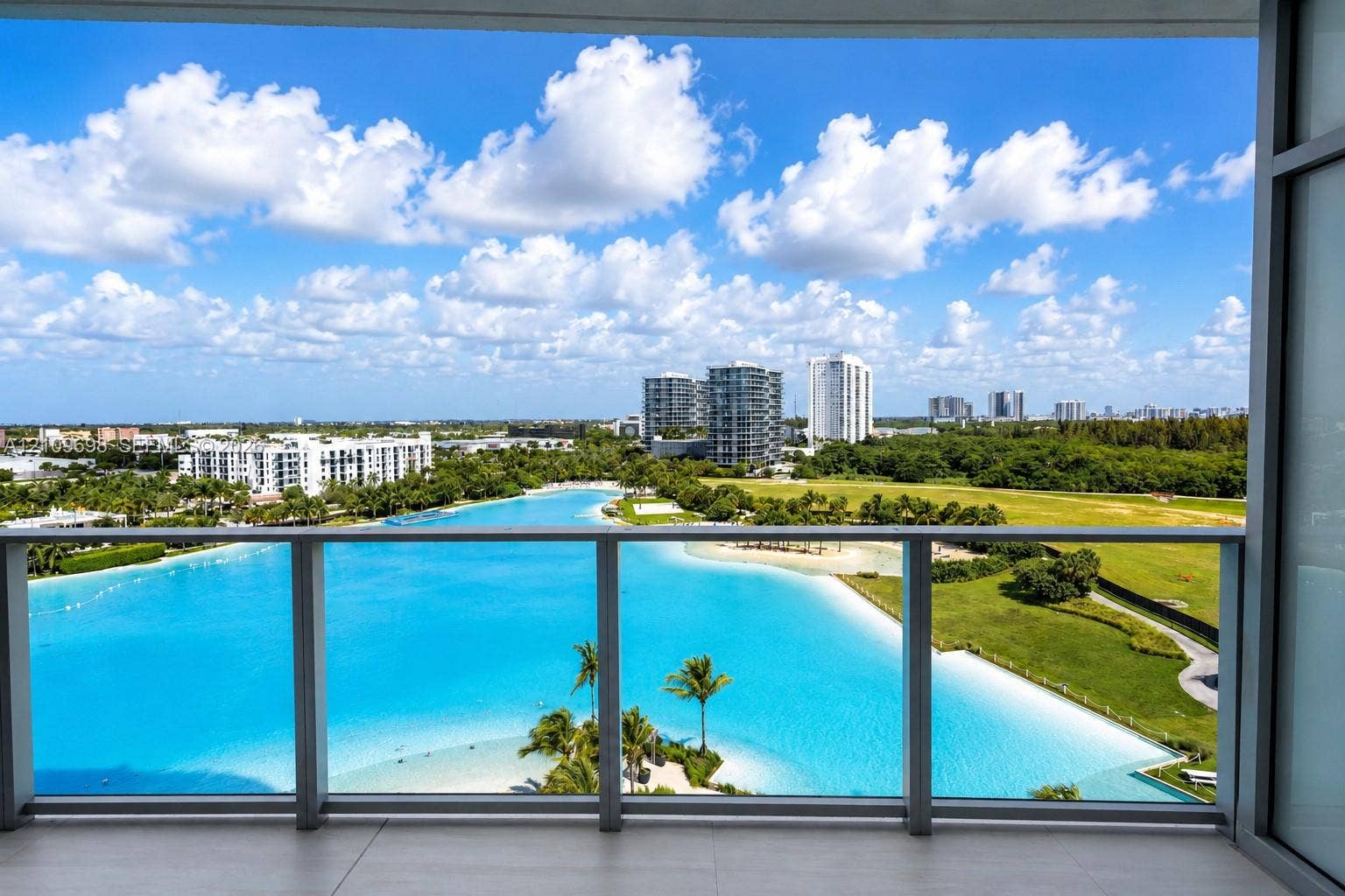 2411 Laguna Circle, #810, North Miami, FL 33181 Covered balcony featuring a glass and metal railing, overlooking an expansive lagoon, sandy shoreline, and palm trees
