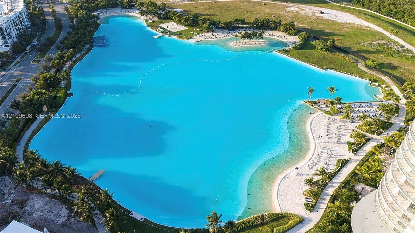 2411 Laguna Circle, #810, North Miami, FL 33181 Expansive turquoise lagoon featuring sandy shorelines, walking paths, landscaped palm trees, and an island formation