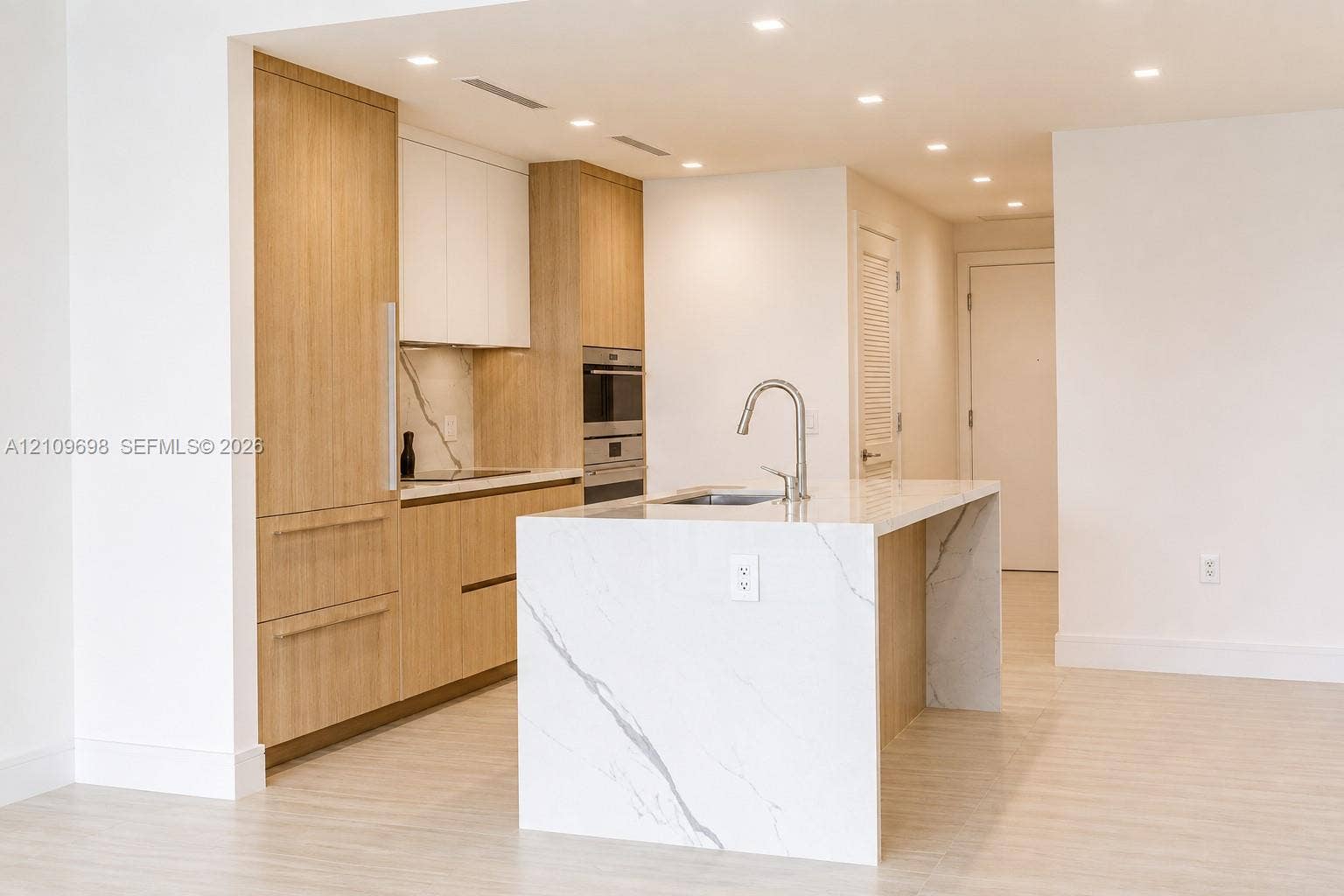 2411 Laguna Circle, #810, North Miami, FL 33181 Kitchen featuring wood-finish cabinetry, stone-style waterfall island, recessed lighting, integrated appliances, and stone-style backsplash