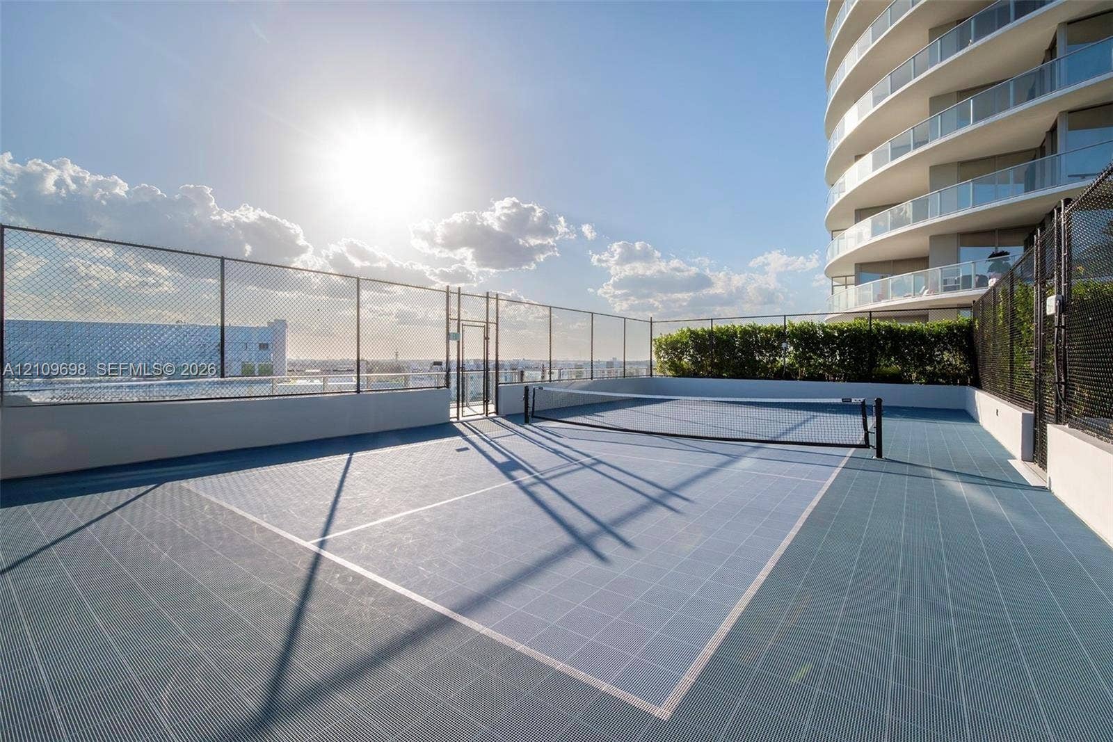 2411 Laguna Circle, #810, North Miami, FL 33181 Rooftop tennis court featuring a modular tile surface, perimeter chain-link fencing, and a built-in privacy hedge