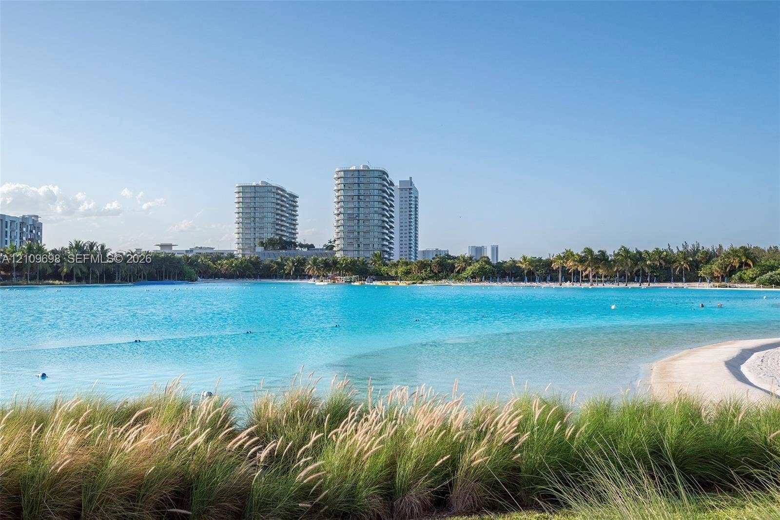 2411 Laguna Circle, #810, North Miami, FL 33181 Expansive lagoon with a sandy beach shoreline, surrounded by tropical landscaping and mature palm trees