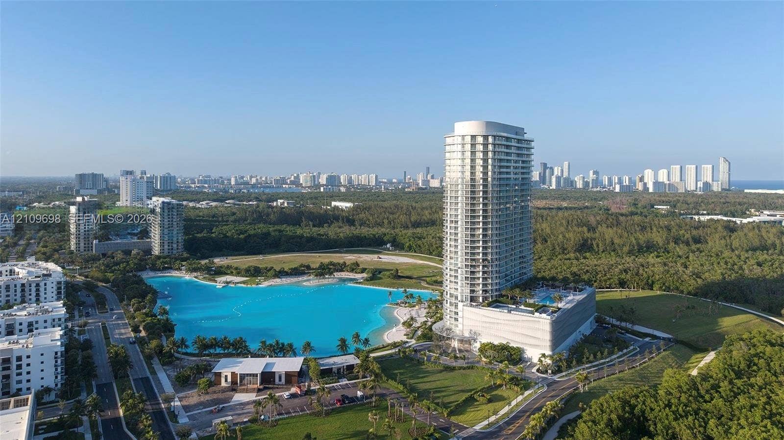 2411 Laguna Circle, #810, North Miami, FL 33181 High-rise tower featuring extensive glass balcony railings, a large-scale lagoon-style pool, surrounding landscaped grounds, and a concrete parking structure