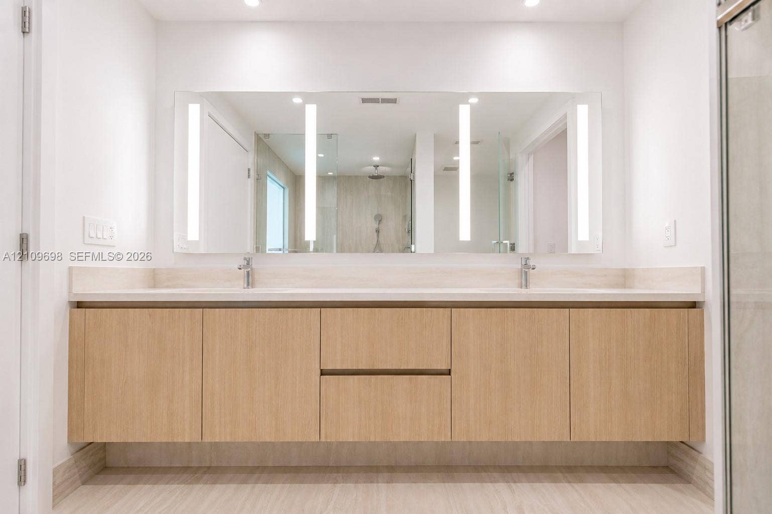 2411 Laguna Circle, #810, North Miami, FL 33181 Floating dual-sink vanity featuring light wood-finish cabinetry, solid surface countertop, integrated LED-lit vanity mirror, and polished chrome fixtures