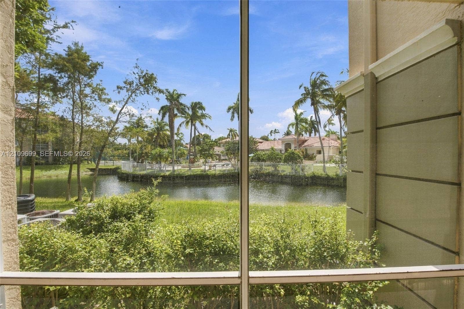 Screen-enclosed outdoor space featuring a water pond, lush landscaping, and palm trees