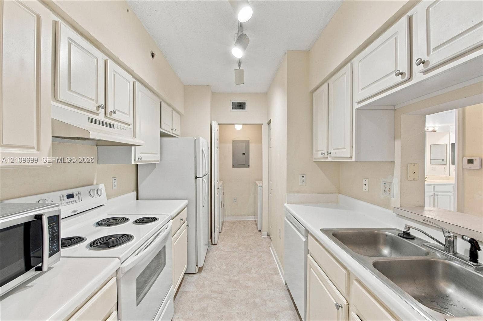 Galley kitchen featuring white cabinetry, solid-surface countertops, dual-basin stainless steel sink, and track lighting