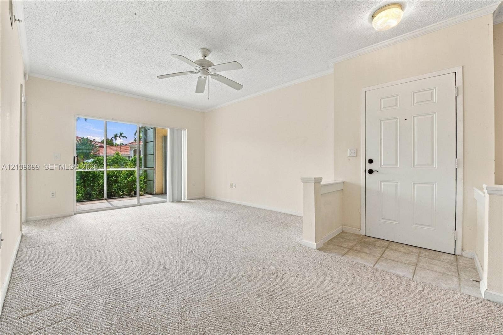 Neutral-toned interior space featuring wall-to-wall carpeting, tile entry flooring, a ceiling fan, and sliding glass doors