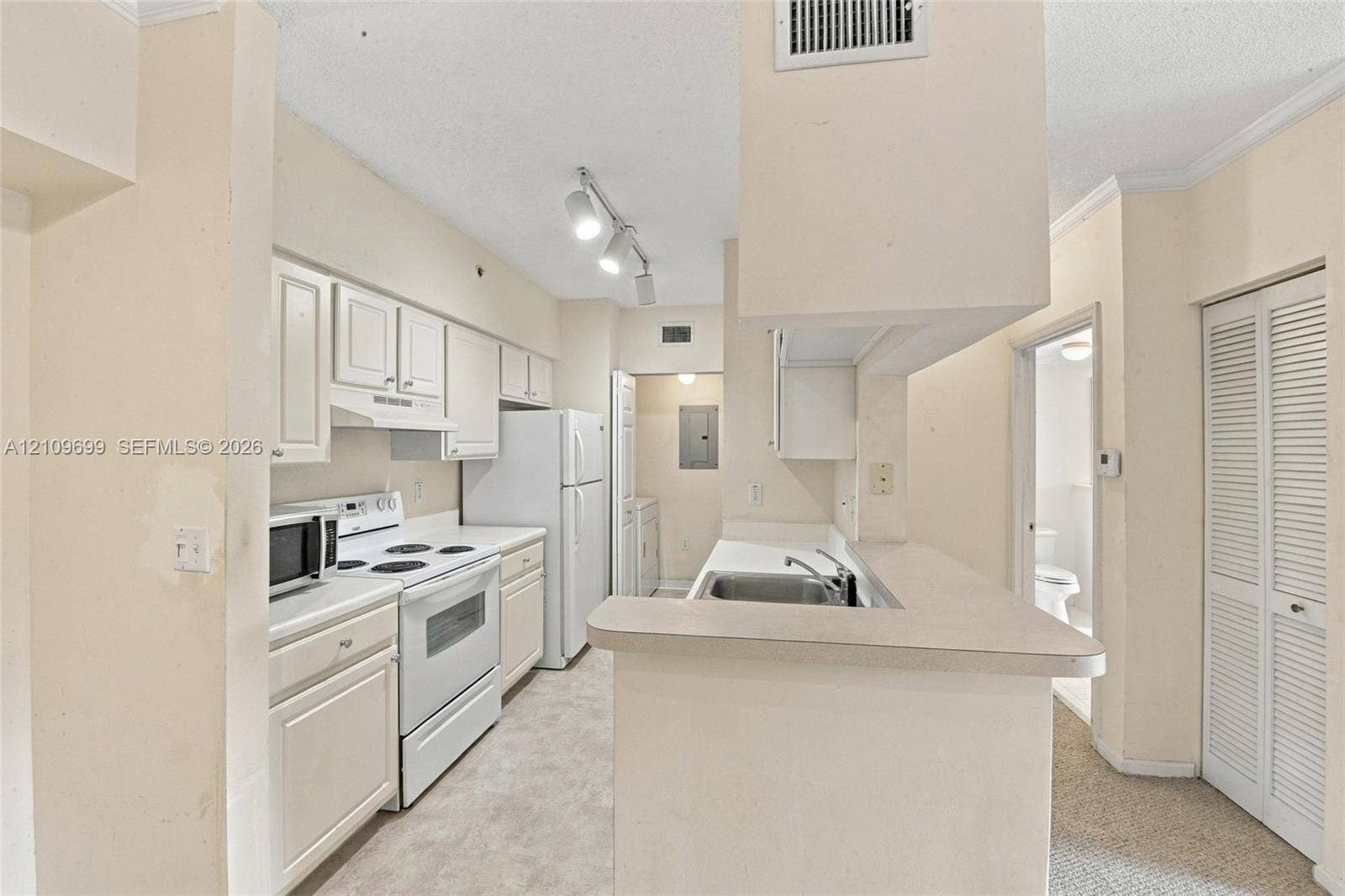 Kitchen featuring white cabinetry, solid-surface countertops, track lighting, a stainless steel dual-basin sink, and louvered bi-fold closet doors