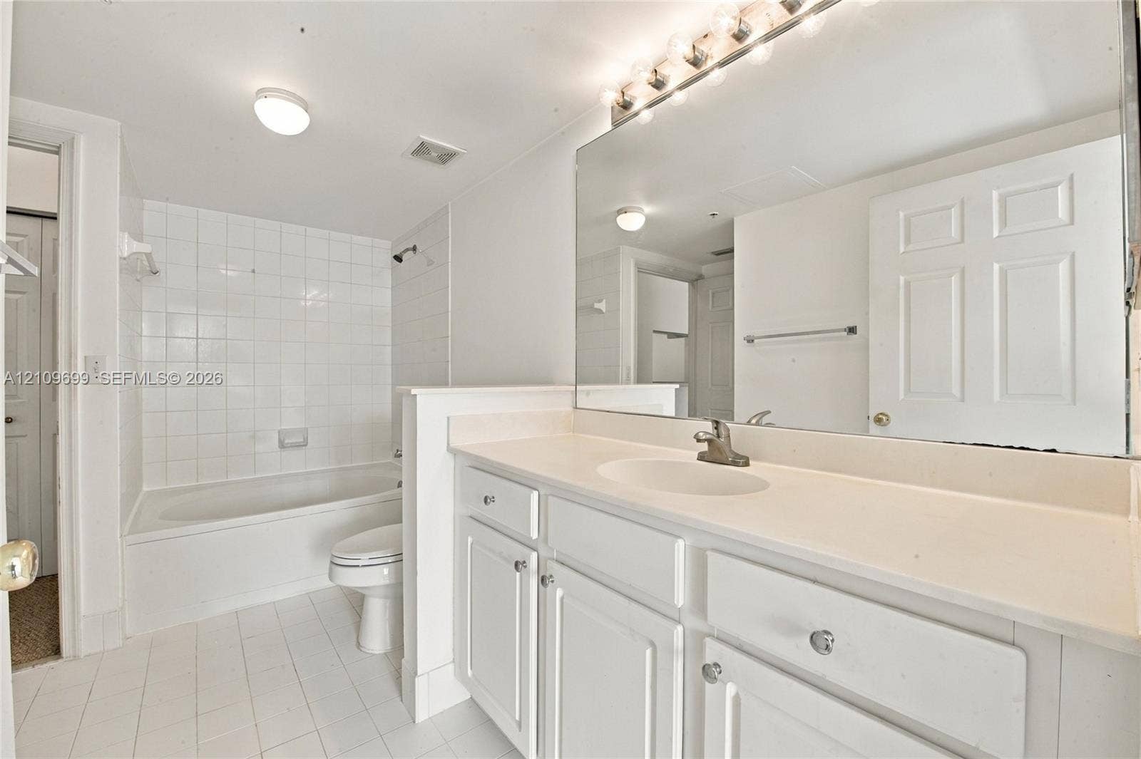 Bathroom featuring a vanity with white cabinetry, a solid surface countertop, an integrated sink, a full-width mirror, and a tiled tub surround