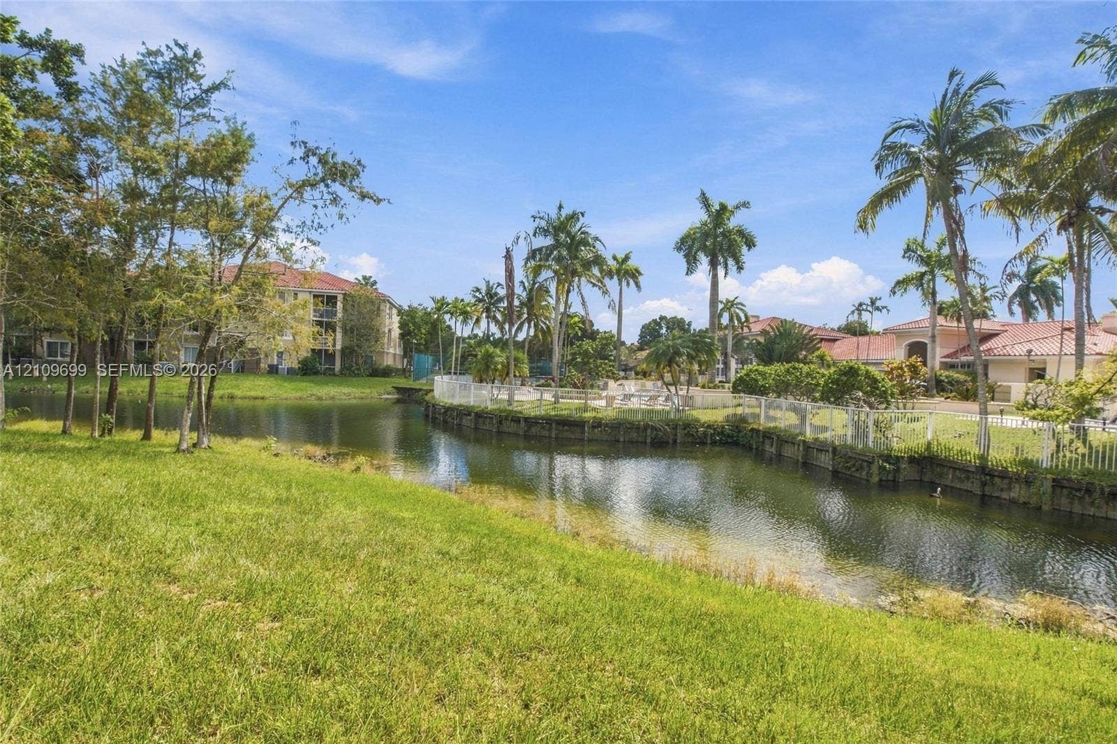 Waterfront grounds featuring a landscaped lawn, mature palm trees, and a retaining wall