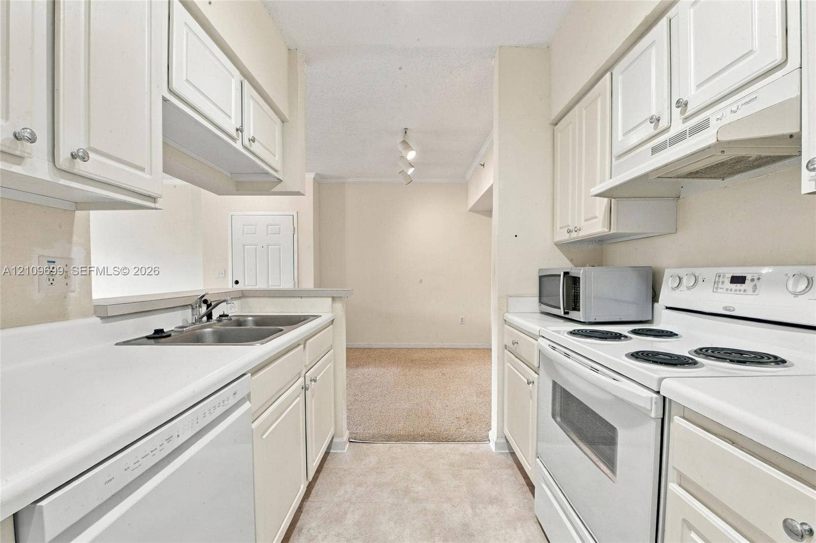 Kitchen featuring white shaker-style cabinetry, solid-surface countertops, dual-basin stainless steel sink, and white appliances