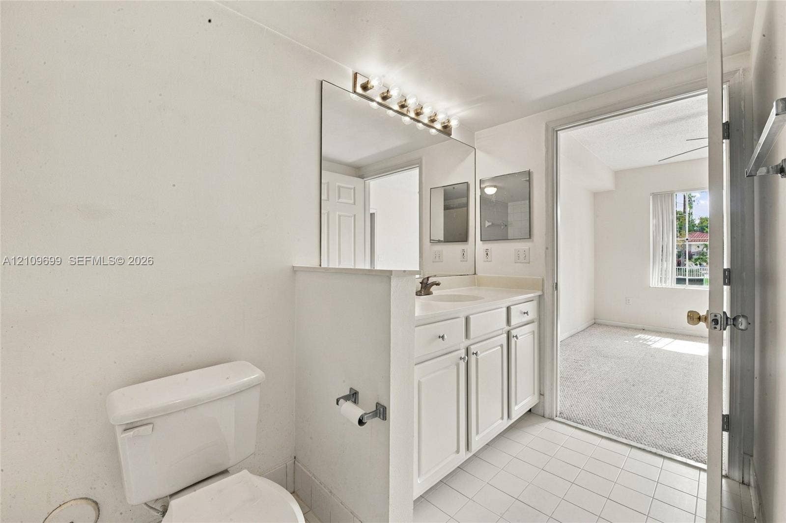 Bathroom featuring white cabinetry, an integrated basin, a wall-mounted light fixture, a large mirror, and tiled flooring