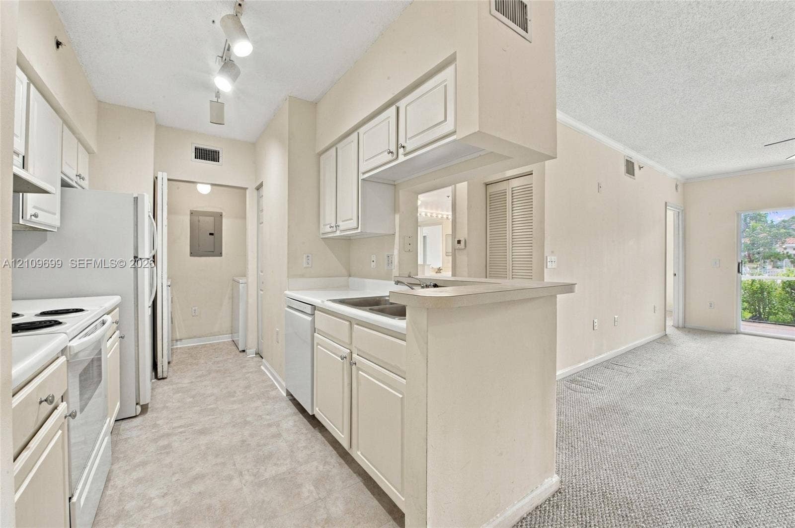 Kitchen featuring white cabinetry, solid-surface countertops, dual-basin stainless steel sink, track lighting, and white appliances