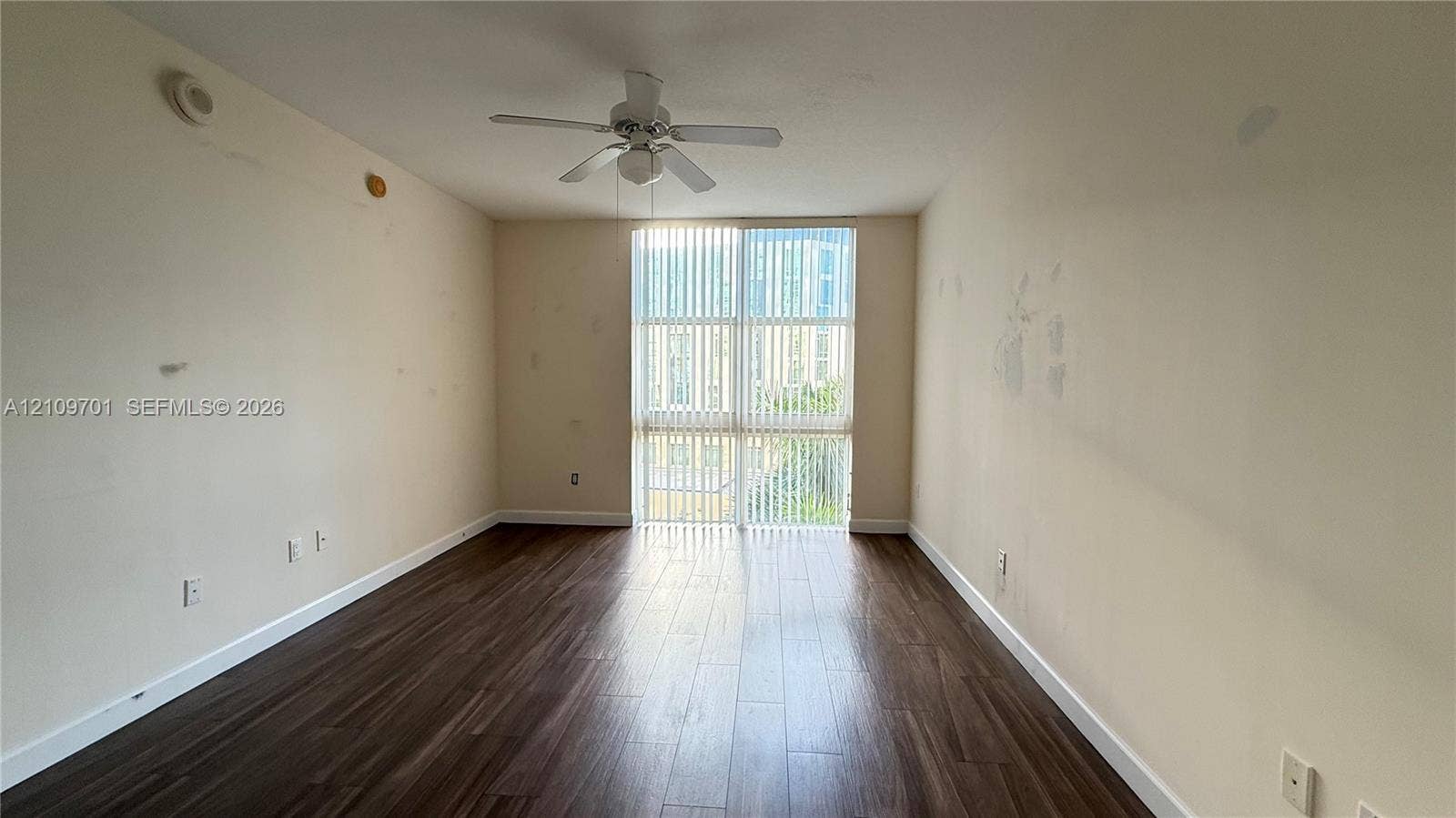 Room featuring wood-finish flooring, a ceiling fan with integrated lighting, and a floor-to-ceiling window assembly with vertical blinds