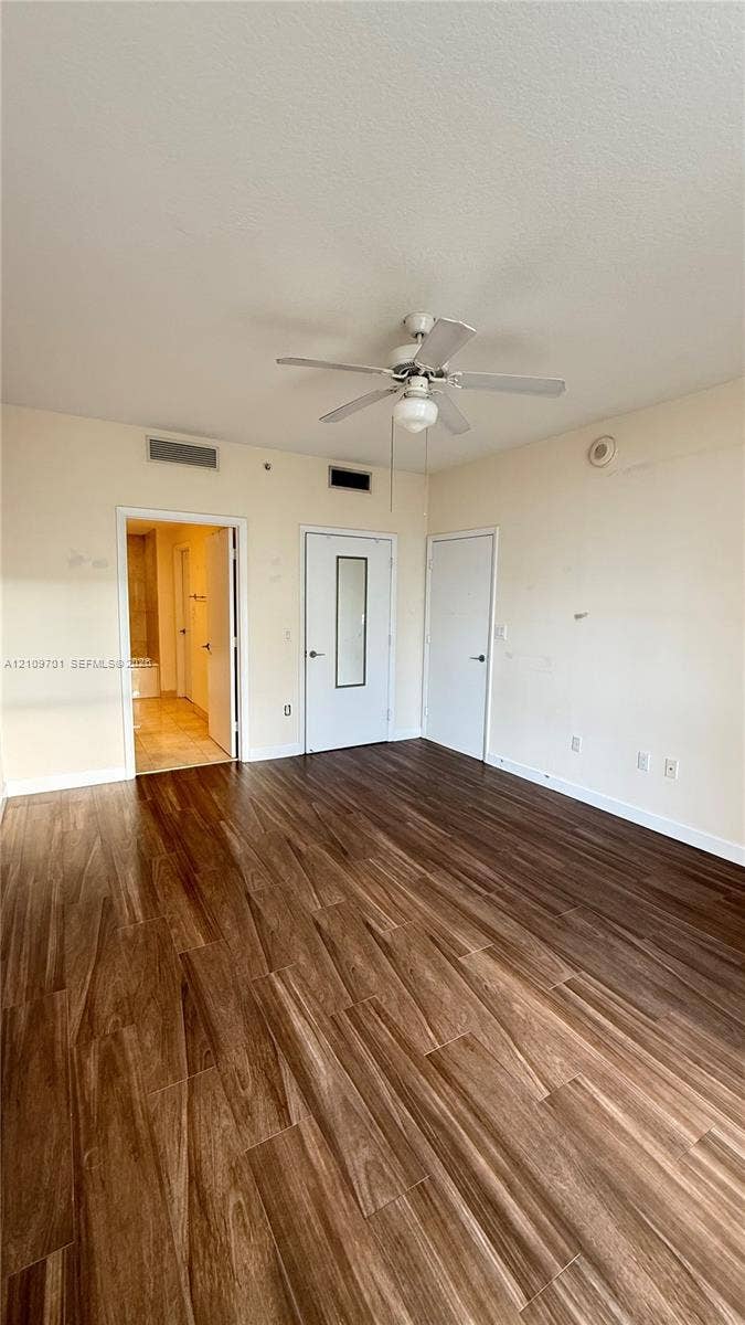 Wood-finish flooring, central ceiling fan with light fixture, and two interior doors, including one with an integrated mirror panel