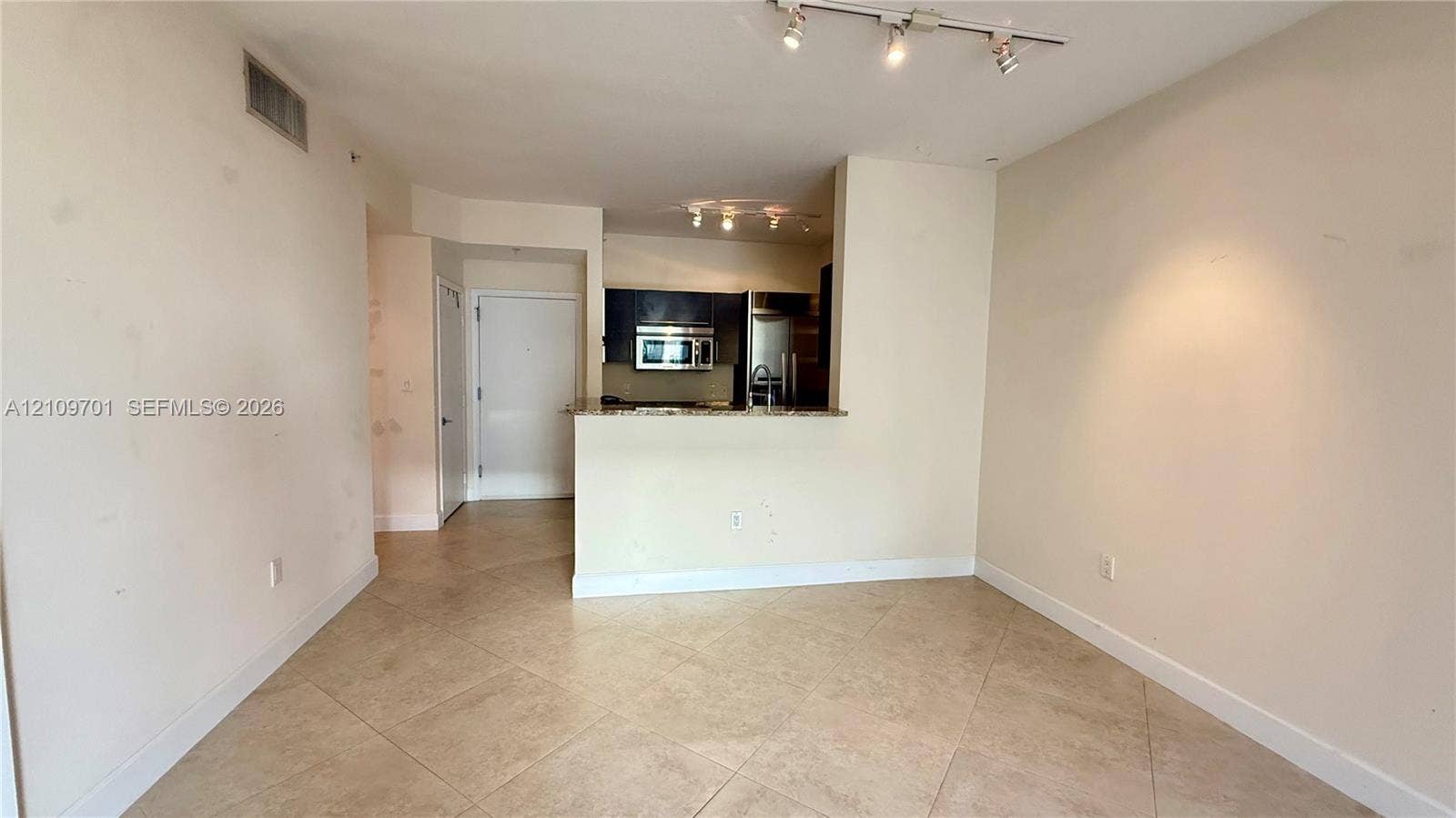 Open-concept area featuring diagonal-set tile flooring, multi-directional track lighting, and a kitchen pass-through counter with stone-surface countertops