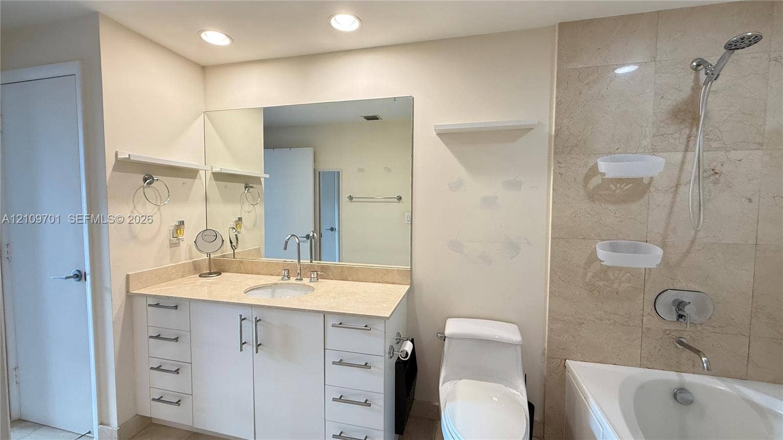 Bathroom featuring a white vanity with drawers, stone-surfaced countertop, large wall-mounted mirror, recessed lighting, and a bathtub with tile surround