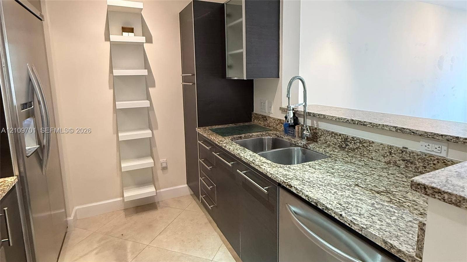 Kitchen featuring stone countertops, stainless steel appliances, dark cabinetry, tile flooring, and integrated shelving
