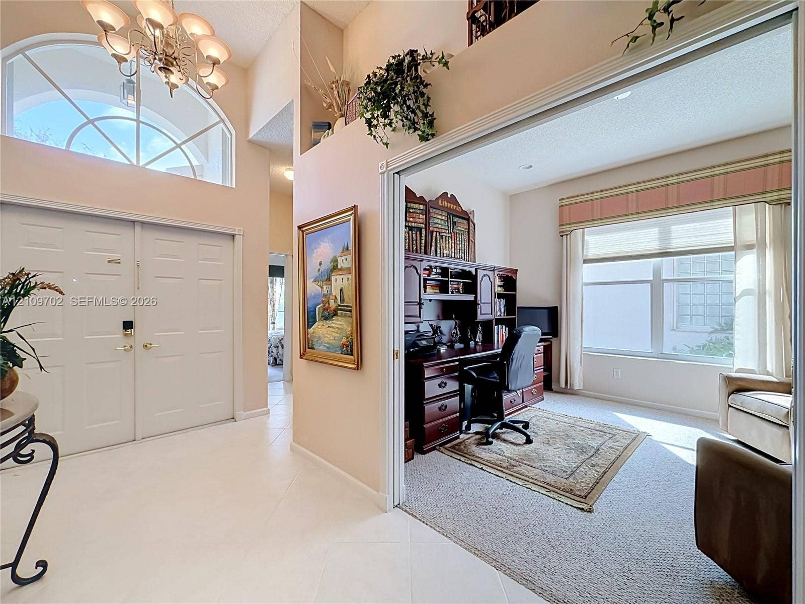 Double-door entryway featuring a multi-pane arched transom window, tile flooring, high ceilings, and a decorative multi-arm chandelier