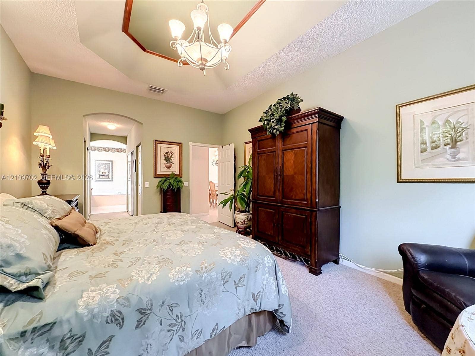 Tray ceiling with a decorative center feature, tiered chandelier, and arched doorway